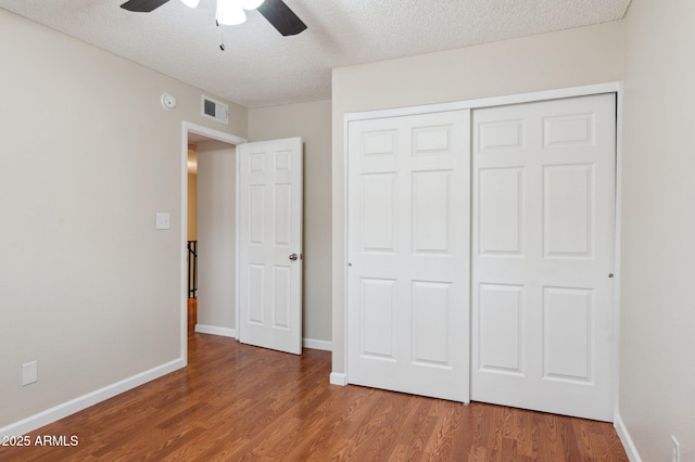 unfurnished bedroom featuring a textured ceiling, wood finished floors, visible vents, baseboards, and a closet