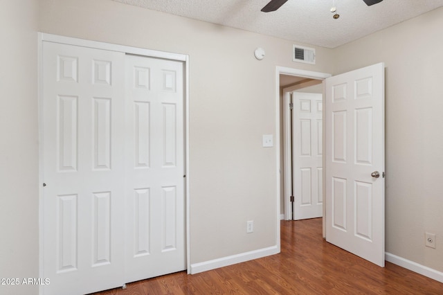 unfurnished bedroom with a textured ceiling, wood finished floors, visible vents, and baseboards