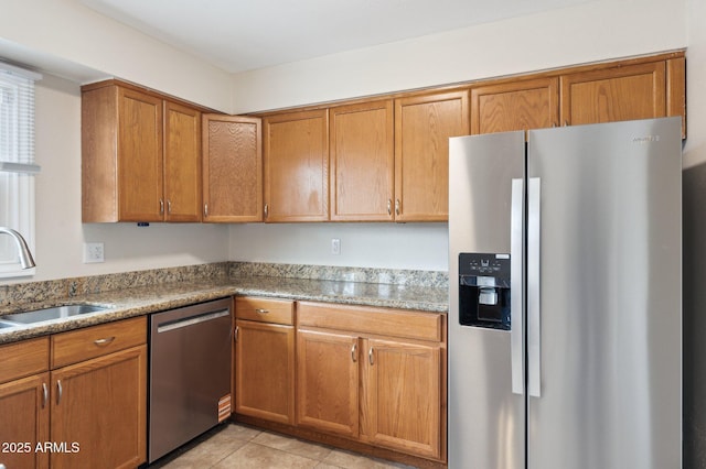 kitchen with light tile patterned floors, appliances with stainless steel finishes, brown cabinetry, and a sink