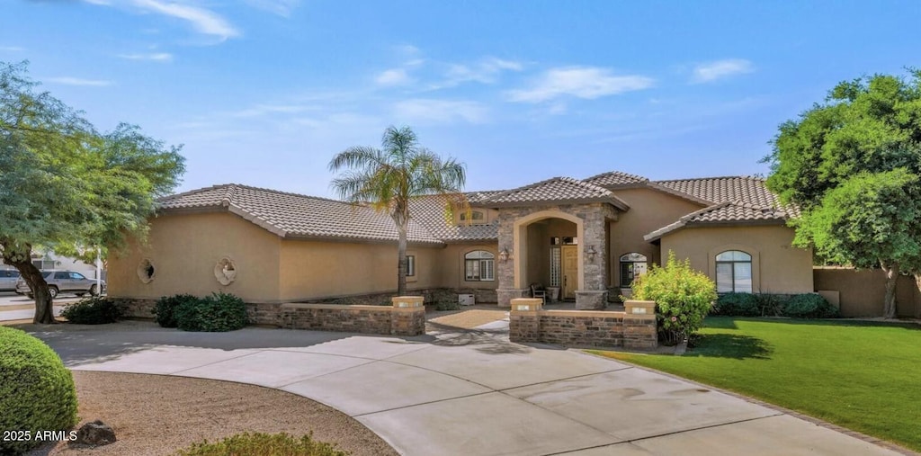 mediterranean / spanish home featuring a front yard, stucco siding, a tile roof, stone siding, and concrete driveway