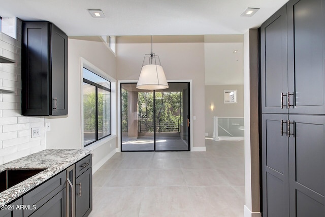 kitchen featuring light stone countertops, decorative light fixtures, tasteful backsplash, and light tile patterned flooring