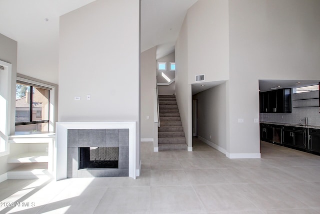 unfurnished living room with a tile fireplace, light tile patterned floors, high vaulted ceiling, and sink