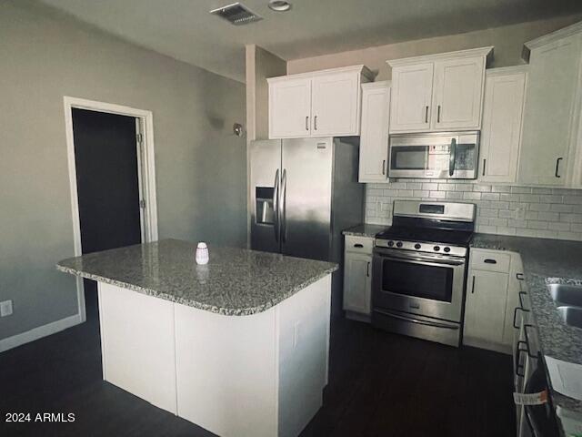 kitchen with a center island, white cabinets, stainless steel appliances, backsplash, and stone countertops