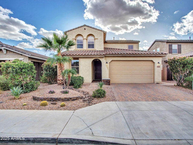 mediterranean / spanish house with a garage, decorative driveway, a tiled roof, and stucco siding