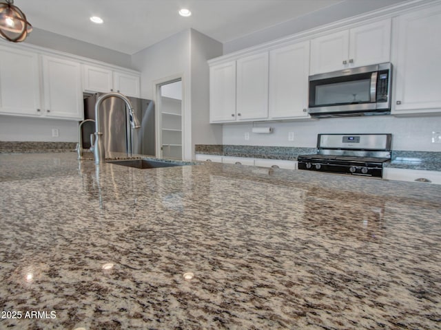 kitchen with appliances with stainless steel finishes, dark stone counters, white cabinetry, and a sink