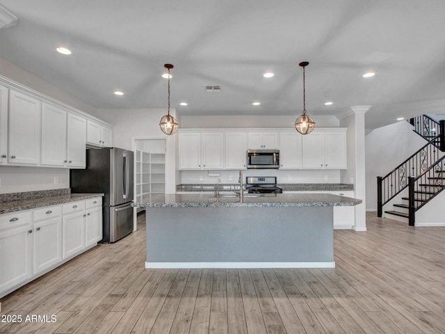 kitchen featuring appliances with stainless steel finishes, white cabinets, an island with sink, and light wood finished floors