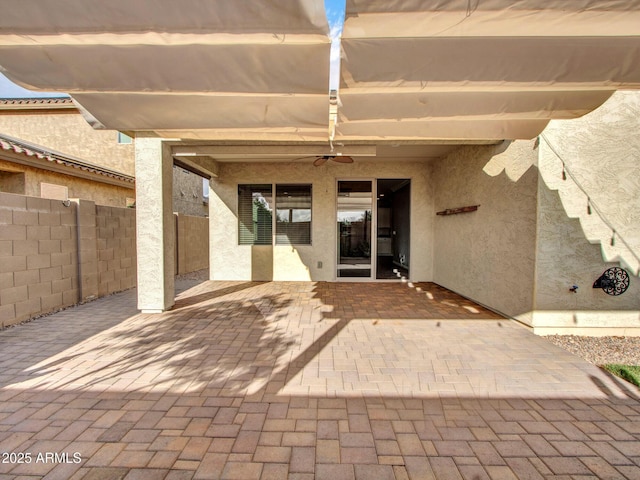 doorway to property featuring ceiling fan, a patio area, fence, and stucco siding