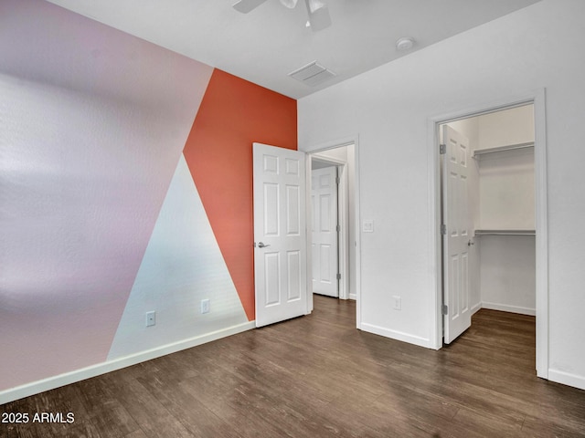 unfurnished bedroom with visible vents, a spacious closet, baseboards, and wood finished floors