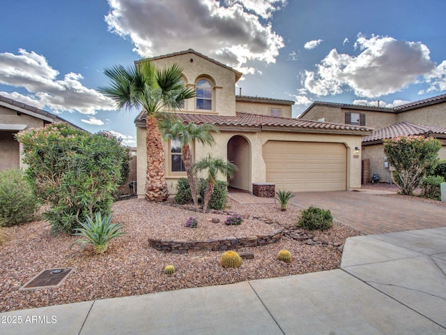 mediterranean / spanish home with an attached garage, a tiled roof, decorative driveway, and stucco siding