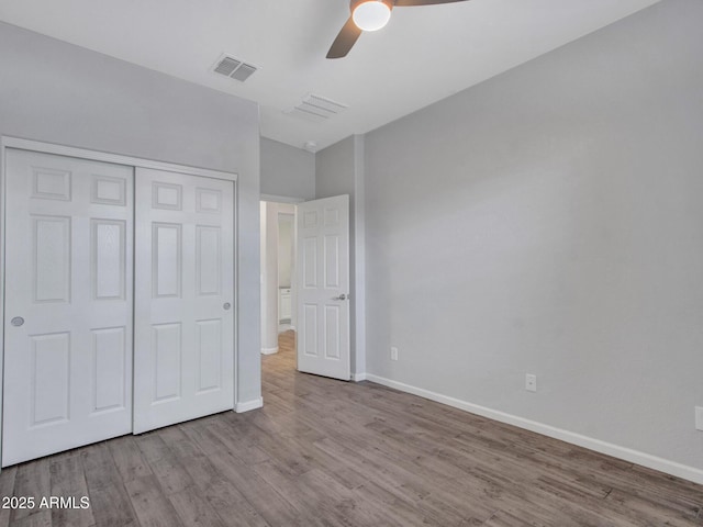 unfurnished bedroom with a closet, visible vents, a ceiling fan, wood finished floors, and baseboards