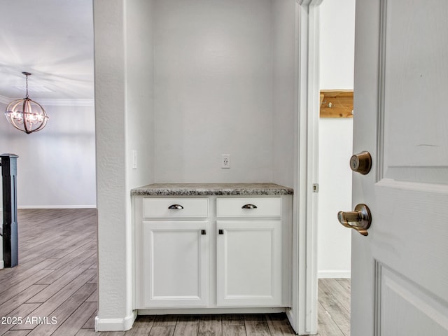 interior space featuring light wood-style flooring, ornamental molding, white cabinets, and baseboards