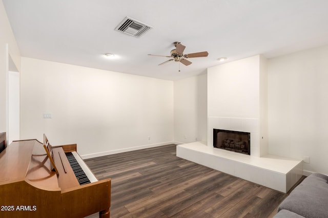 living room featuring a tiled fireplace, visible vents, dark wood-type flooring, and baseboards