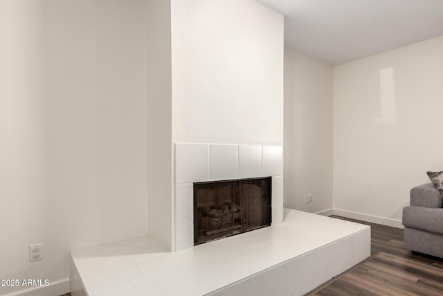 living room featuring baseboards, wood finished floors, and a tiled fireplace