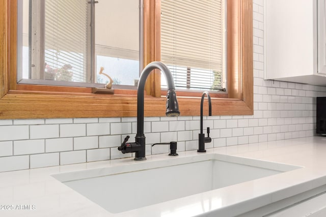 interior details with tasteful backsplash, white cabinetry, light countertops, and a sink