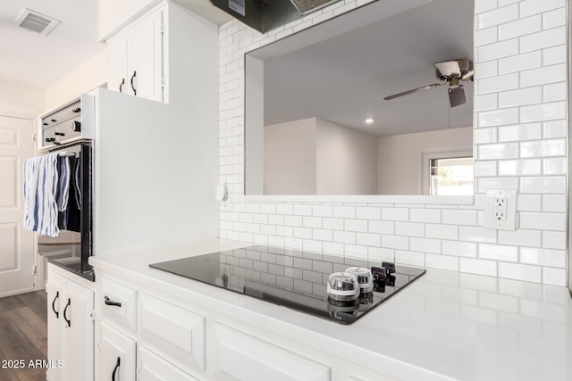 kitchen featuring visible vents, a ceiling fan, tasteful backsplash, white cabinets, and black electric stovetop