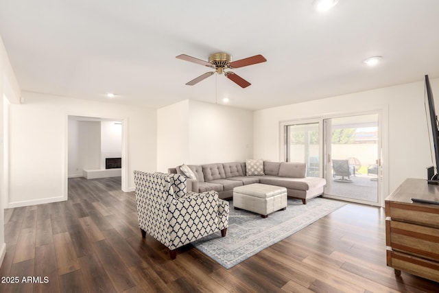 living area featuring dark wood-type flooring, a fireplace with raised hearth, recessed lighting, baseboards, and ceiling fan