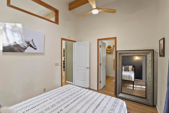 bedroom featuring ceiling fan, beamed ceiling, light hardwood / wood-style floors, and a high ceiling