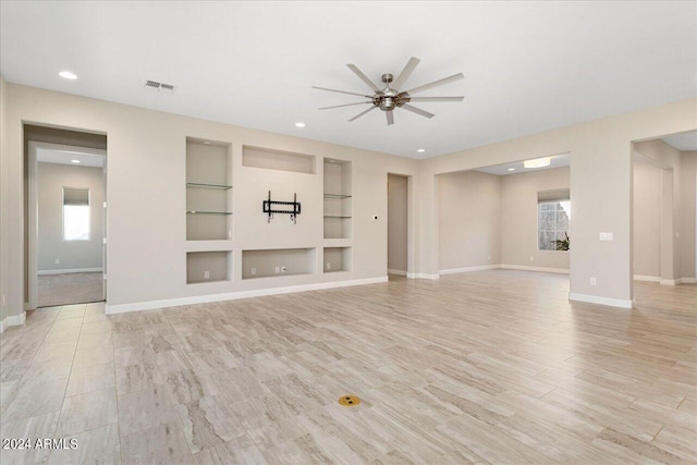 unfurnished living room with built in shelves, light hardwood / wood-style floors, and ceiling fan