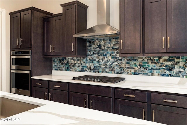 kitchen with dark brown cabinets, stainless steel appliances, tasteful backsplash, and wall chimney range hood