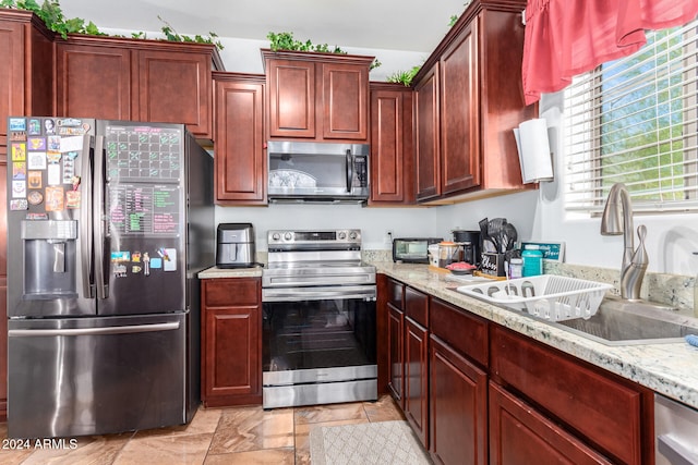 kitchen with appliances with stainless steel finishes, light stone countertops, and sink