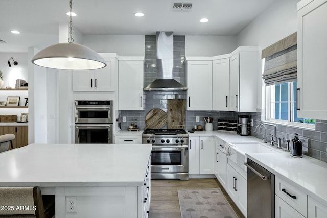 kitchen featuring visible vents, decorative backsplash, appliances with stainless steel finishes, wall chimney exhaust hood, and a sink