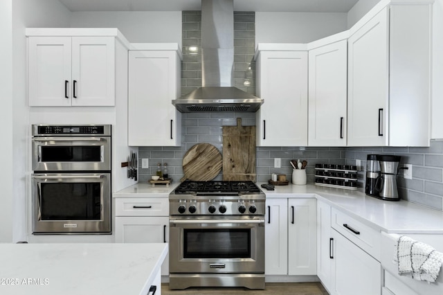 kitchen featuring light countertops, wall chimney range hood, tasteful backsplash, and appliances with stainless steel finishes