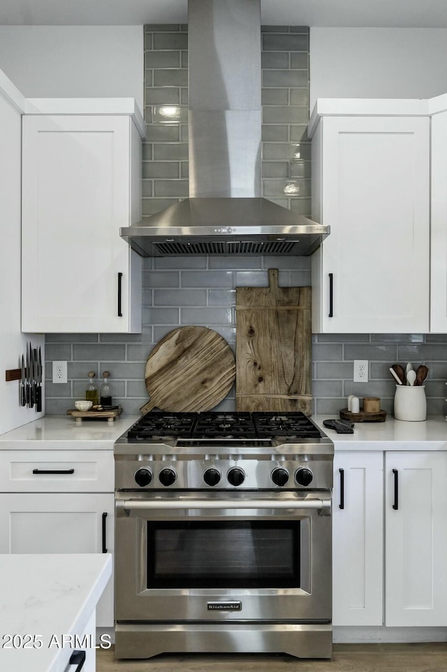 kitchen with decorative backsplash, wall chimney exhaust hood, white cabinets, and high end stainless steel range