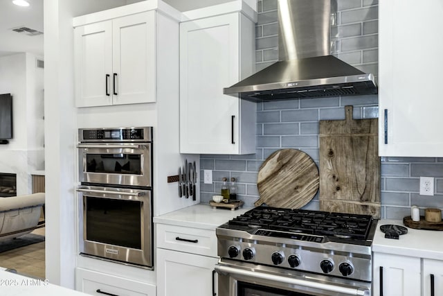 kitchen with decorative backsplash, wall chimney range hood, white cabinetry, and stainless steel appliances