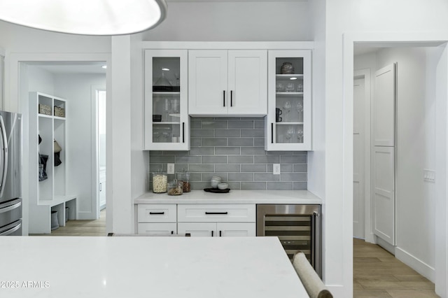 kitchen with beverage cooler, freestanding refrigerator, light countertops, white cabinets, and backsplash