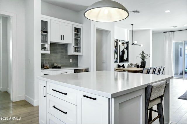 kitchen featuring visible vents, glass insert cabinets, light countertops, decorative backsplash, and light wood-style flooring