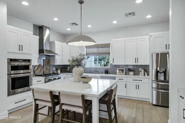 kitchen featuring light countertops, wall chimney range hood, visible vents, and appliances with stainless steel finishes