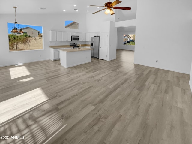 kitchen featuring stainless steel appliances, white cabinets, pendant lighting, sink, and a kitchen island with sink