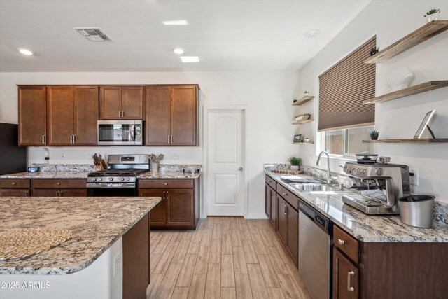 2335 W Sunland Ave, Phoenix, AZ 85041 - kitchen with open shelves, appliances with stainless steel finishes, a sink, light wood-style flooring, and light stone counters