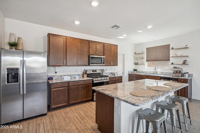 2335 W Sunland Ave, Phoenix, AZ 85041 - kitchen with appliances with stainless steel finishes, open shelves, light wood finished floors, a kitchen bar, and recessed lighting