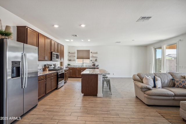 2335 W Sunland Ave, Phoenix, AZ 85041 - kitchen with appliances with stainless steel finishes, open floor plan, open shelves, a kitchen bar, and light wood-type flooring
