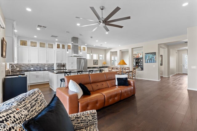 living room featuring a healthy amount of sunlight, ceiling fan, sink, and dark wood-type flooring