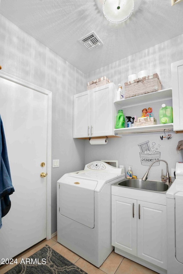 laundry area with cabinets, a textured ceiling, sink, washing machine and clothes dryer, and light tile patterned floors