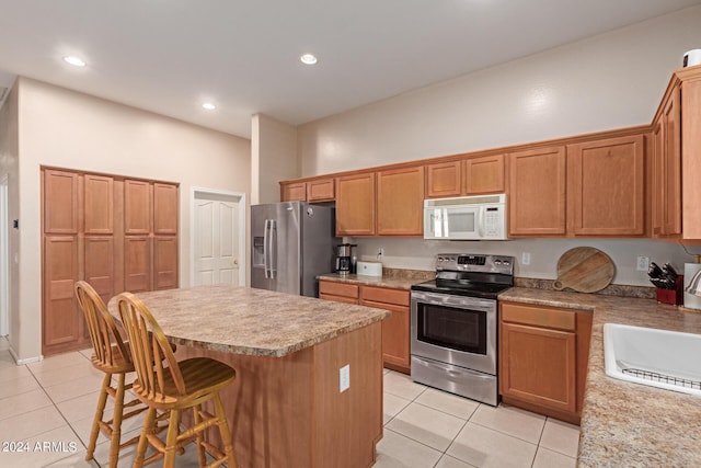 kitchen featuring light tile patterned floors, a sink, appliances with stainless steel finishes, a kitchen breakfast bar, and a kitchen island