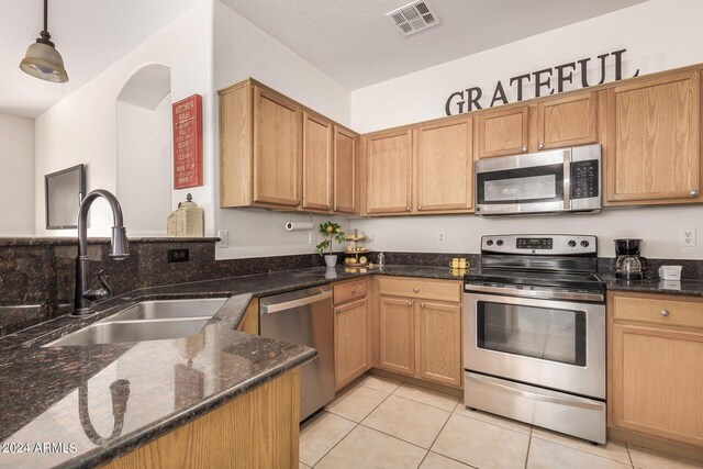 kitchen featuring sink, hanging light fixtures, stainless steel appliances, dark stone counters, and light tile patterned floors