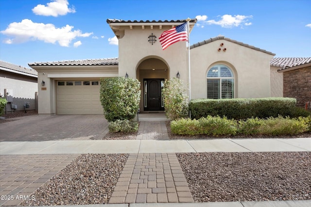 mediterranean / spanish-style home with decorative driveway, a tiled roof, an attached garage, and stucco siding