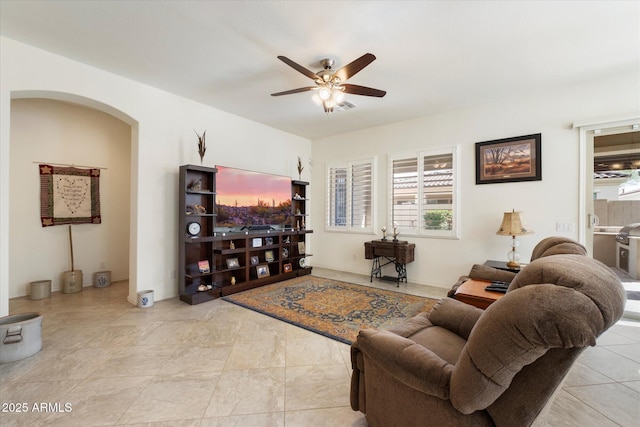 living room featuring light tile patterned floors, arched walkways, and a ceiling fan