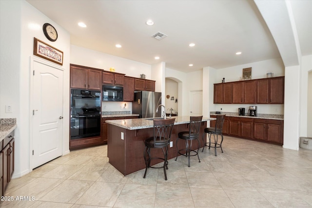 kitchen with visible vents, a kitchen island with sink, a sink, black appliances, and a kitchen bar