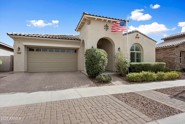 mediterranean / spanish-style house featuring an attached garage, a tiled roof, decorative driveway, and stucco siding