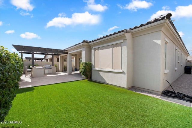 rear view of property with a lawn, a tiled roof, area for grilling, and stucco siding