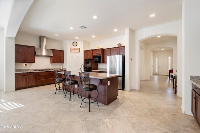 kitchen with arched walkways, a breakfast bar, visible vents, appliances with stainless steel finishes, and wall chimney exhaust hood