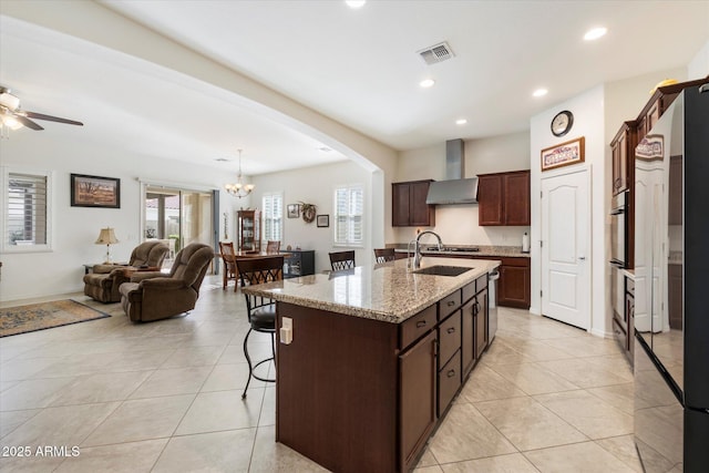 kitchen featuring visible vents, arched walkways, wall chimney exhaust hood, a breakfast bar area, and a sink