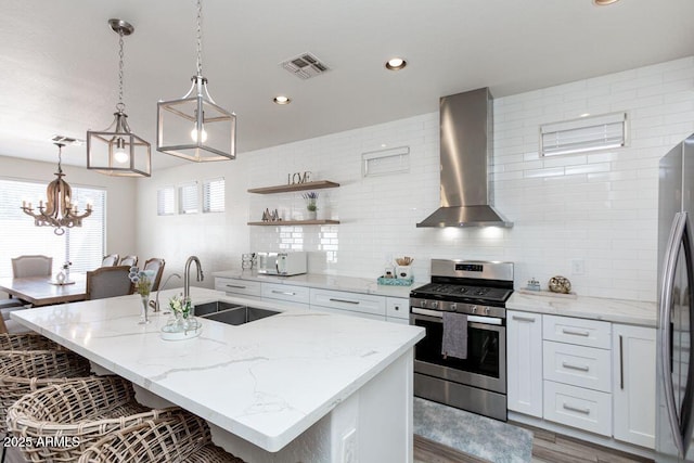 kitchen with white cabinetry, appliances with stainless steel finishes, wall chimney range hood, and an island with sink