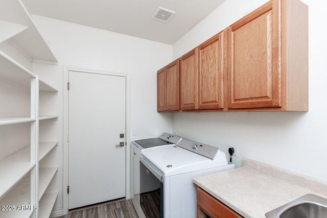 clothes washing area with independent washer and dryer, wood-type flooring, and cabinets