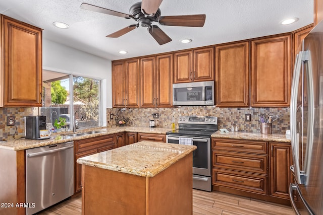 kitchen featuring stainless steel appliances, a center island, light wood-type flooring, light stone counters, and sink