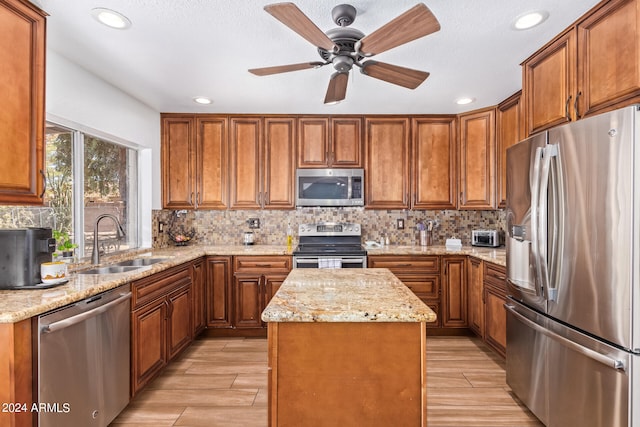 kitchen with appliances with stainless steel finishes, backsplash, light stone countertops, a kitchen island, and sink